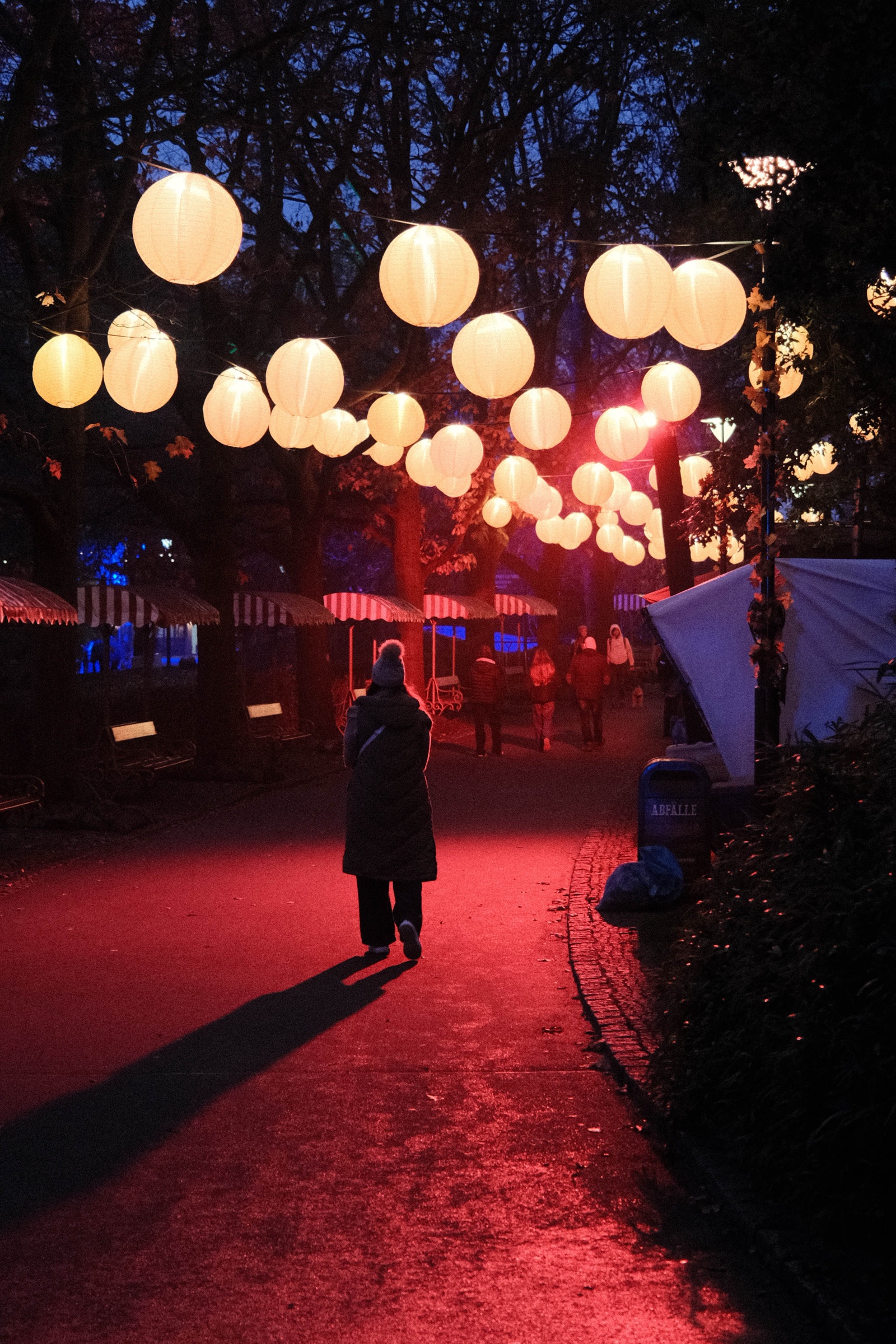 A lone figure walking beneath glowing carnival lights at night