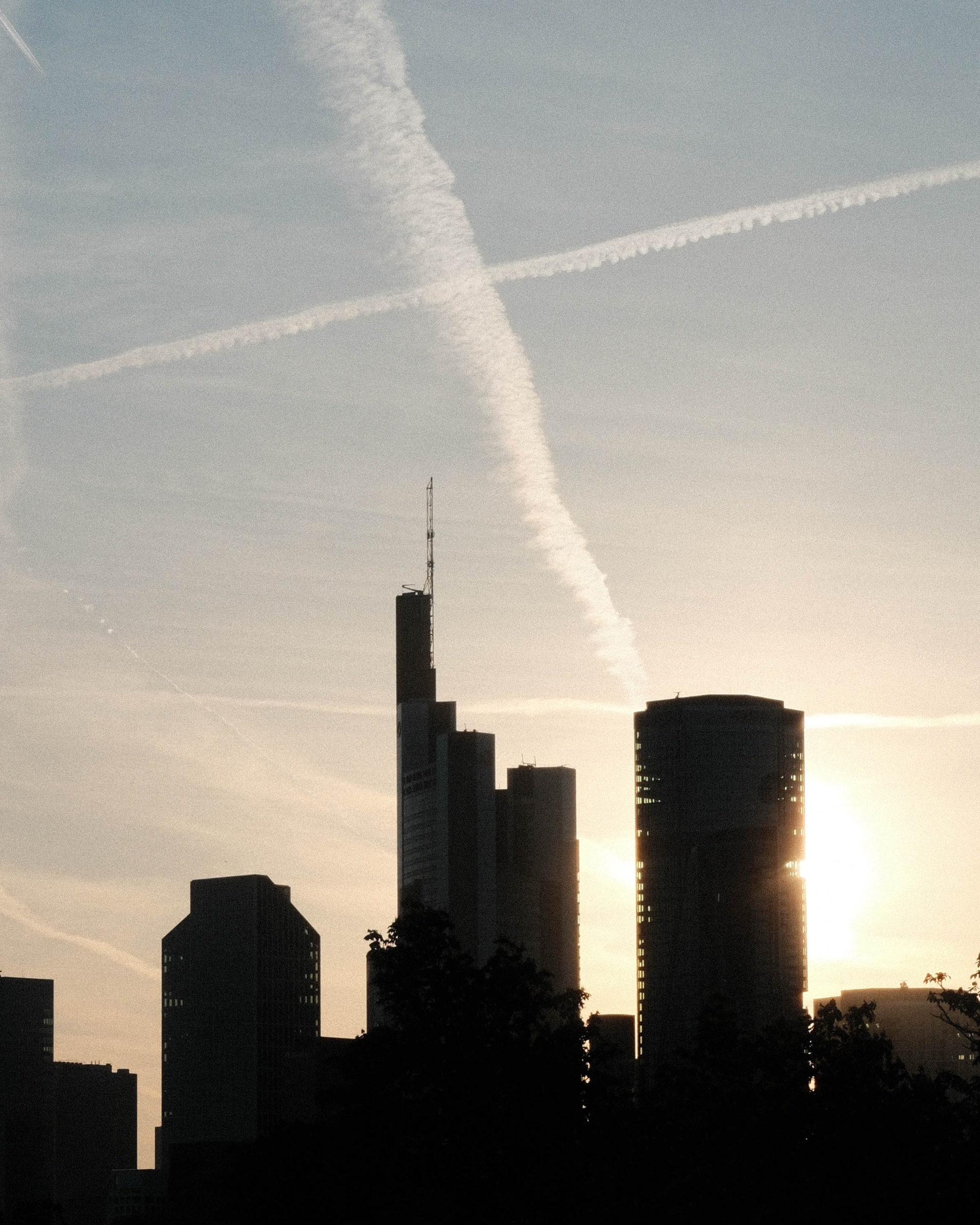 Frankfurt skyline beneath intersecting aircraft contrails