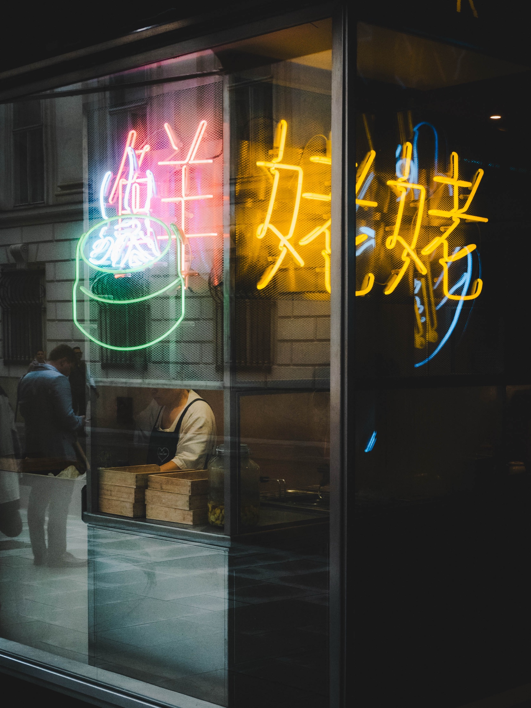 Colourful neon signs reflected in a dark shop window