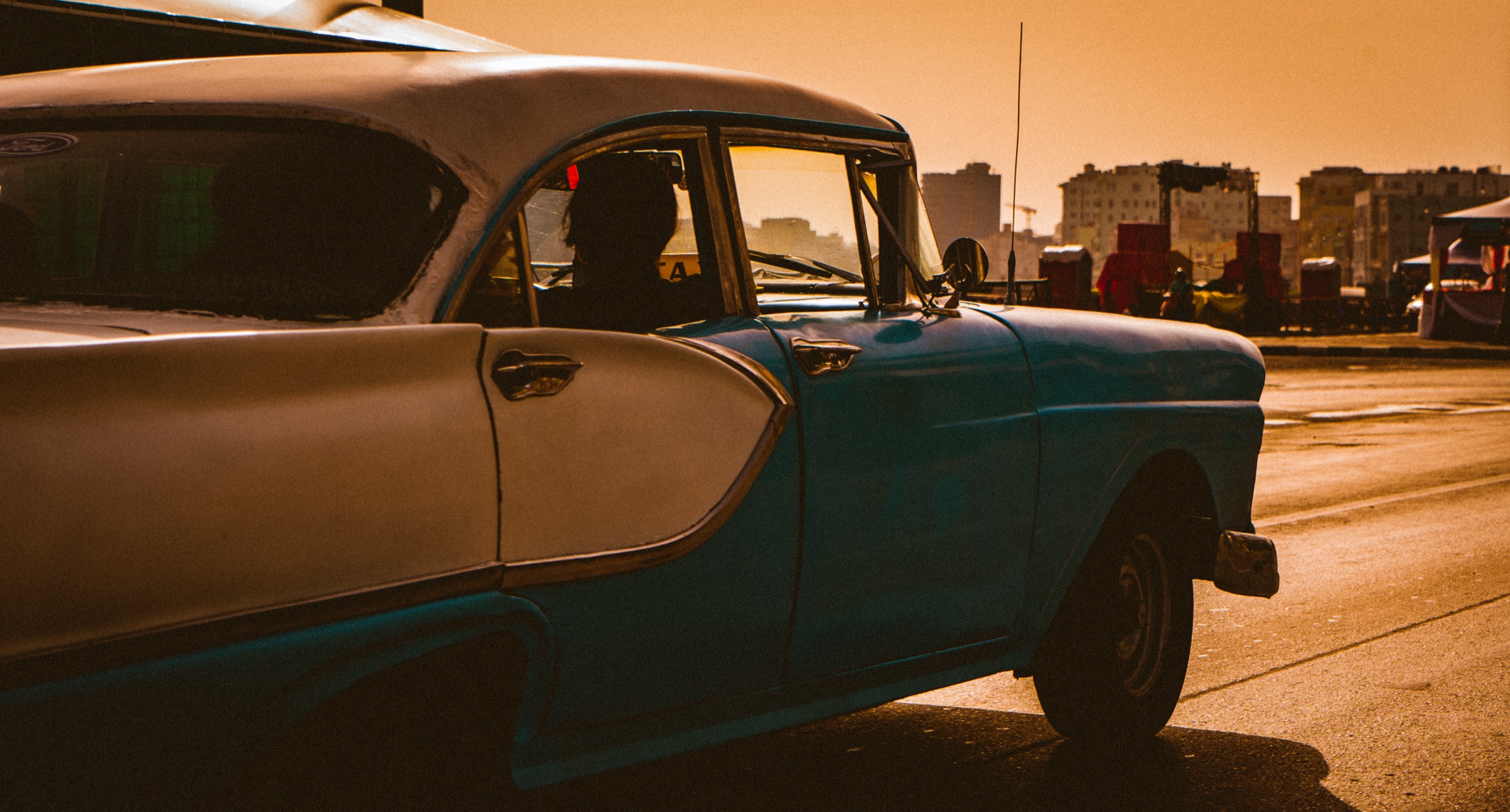 Classic American car driving through warm evening light in Cuba