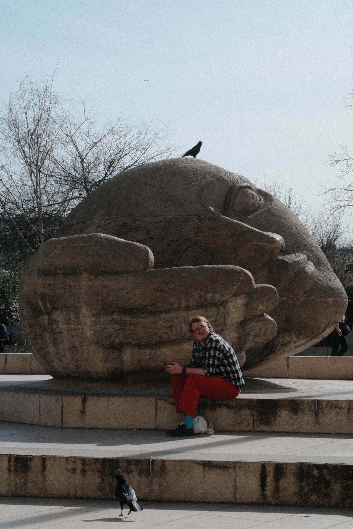 A seated figure beneath a monumental stone sculpture