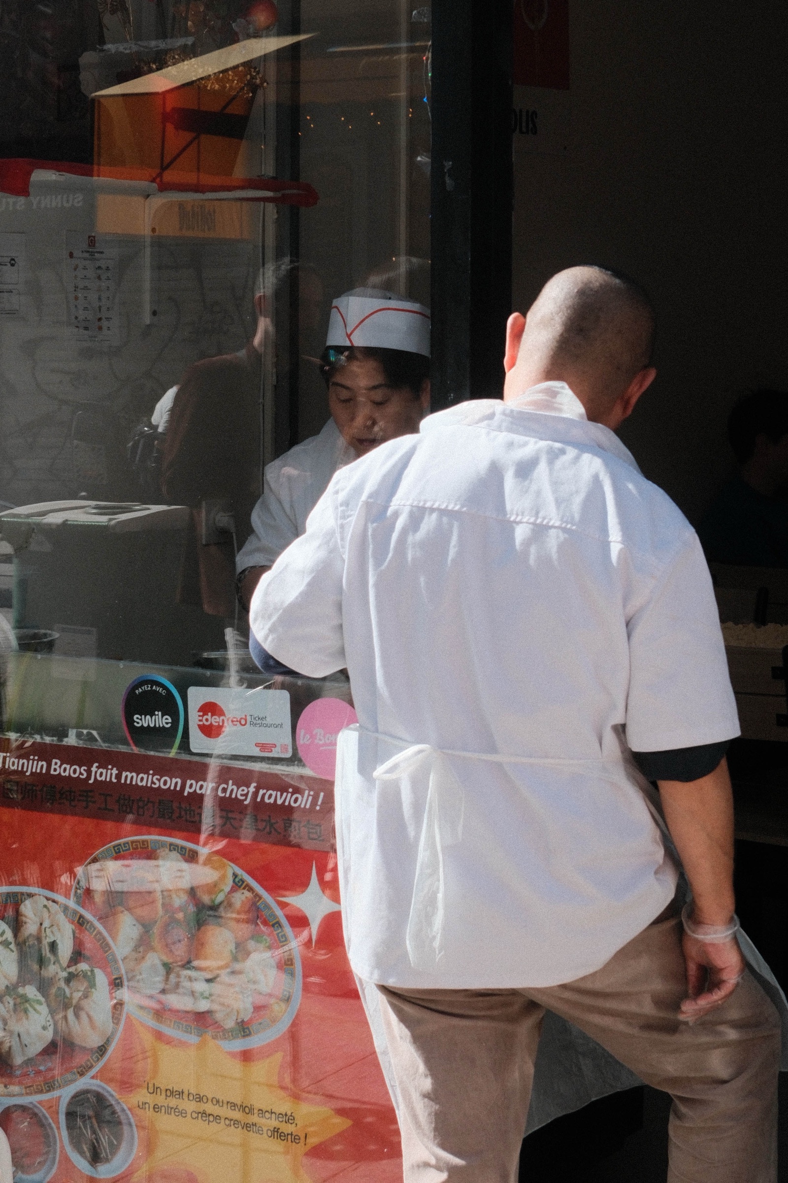 Two men standing beside a sunlit storefront window
