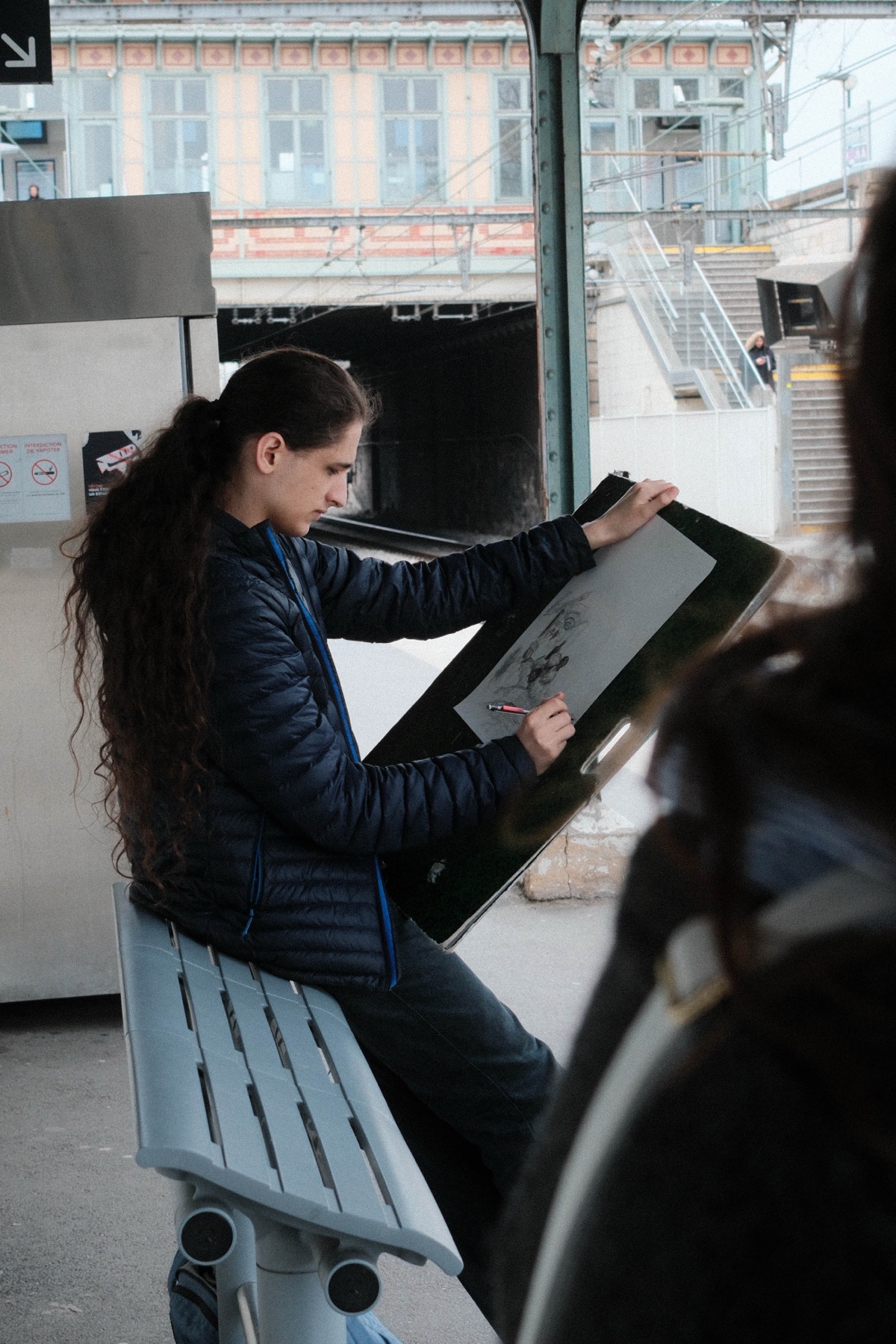 A young woman sketching while waiting on a train platform